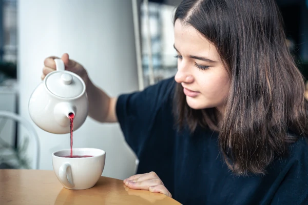 woman pours tea from a teapot with theine not caffeine